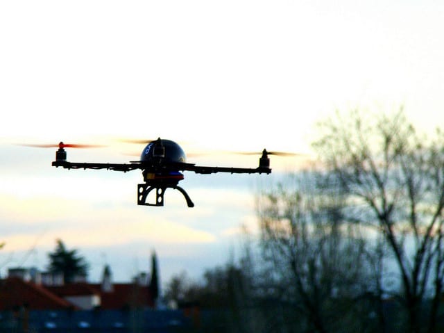 A small black drone hovering above a bustling city.