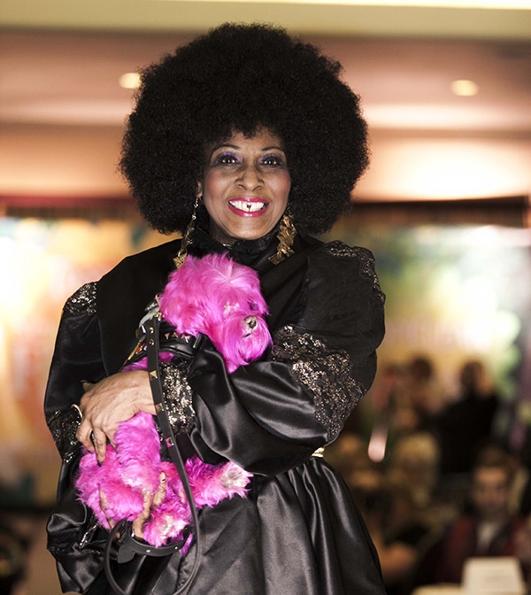 A woman in a black dress holding a pink teddy bear at the New York Pet Fashion Show.