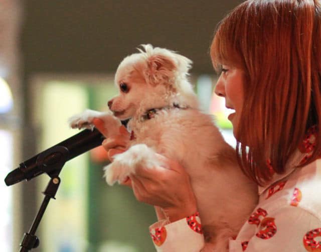 Two girls holding a small white dog in front of a microphone.