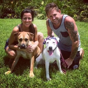 A bonnet-wearing pit bull and their owners posing for a photo.