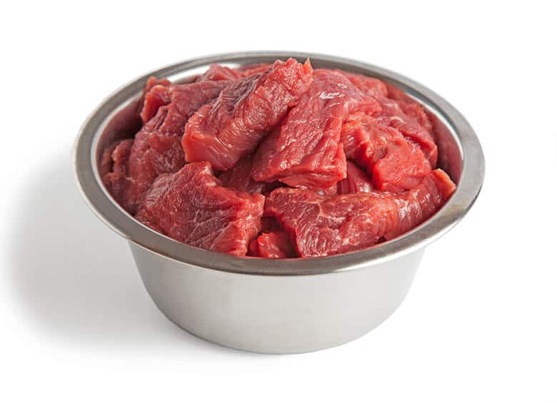 Raw beef in a metal bowl on a white background, suitable for dog's raw diet.