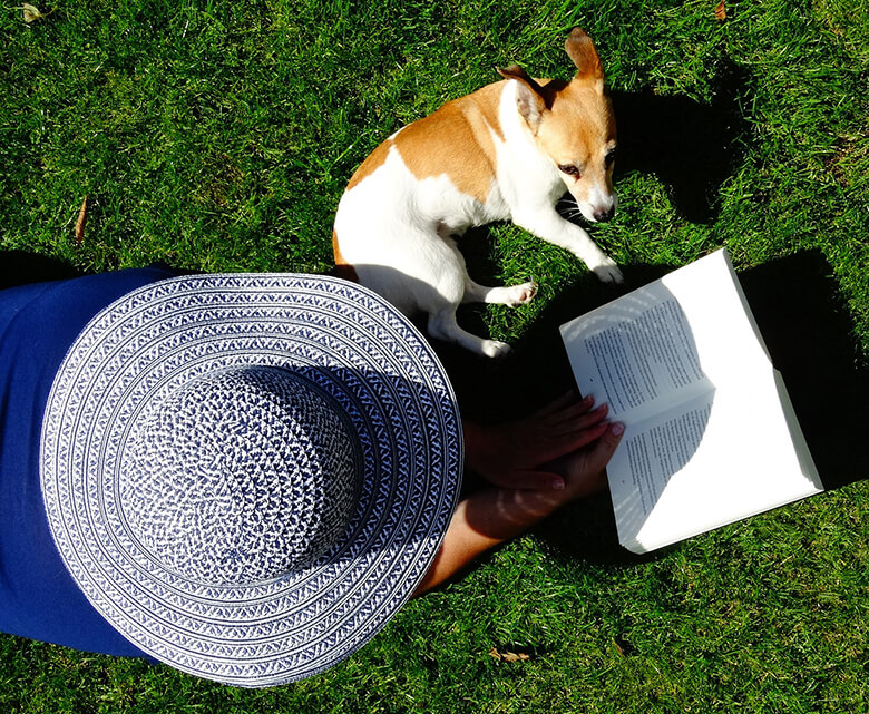 A woman in a hat reading a book series to her dog, who stays calm while home alone.