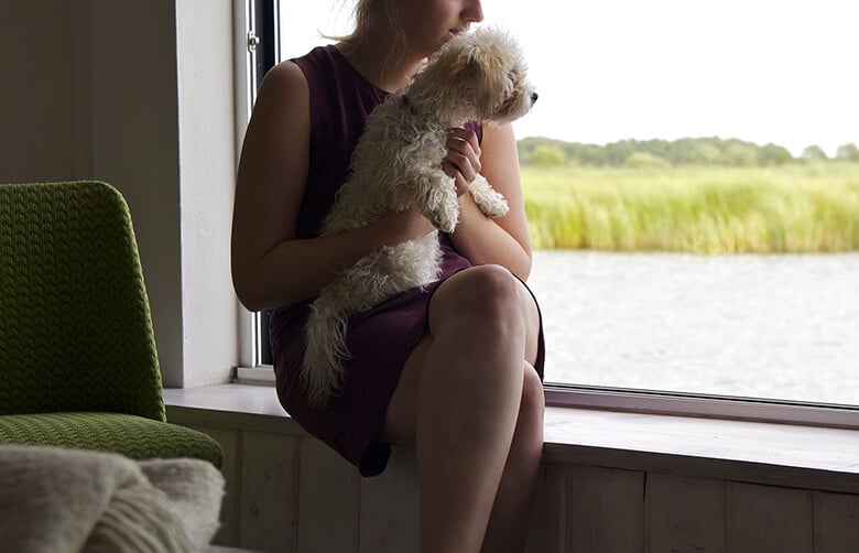 A woman sitting on a window sill in New York City, gracefully holding a small white dog while she assists victims.