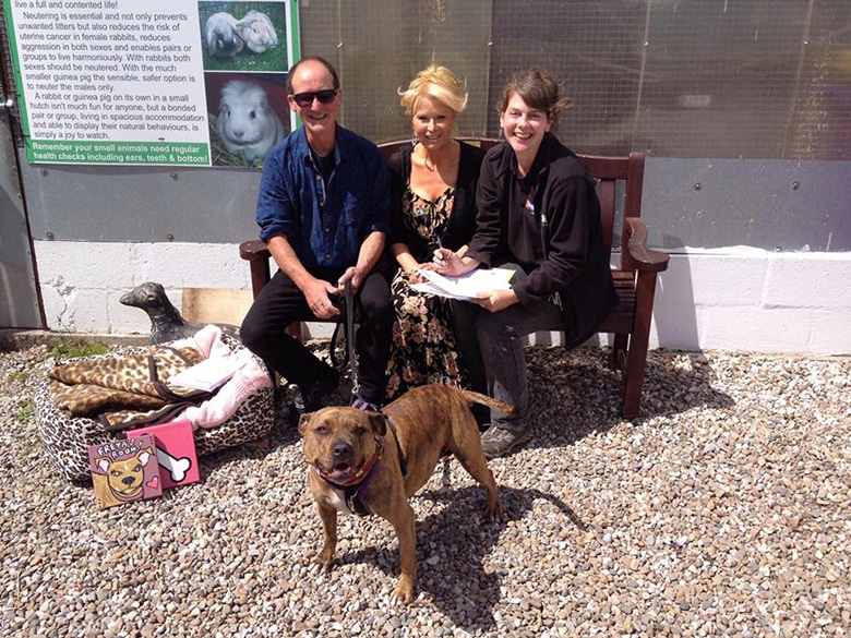 A woman and a man sitting on a bench with their adopted dog.