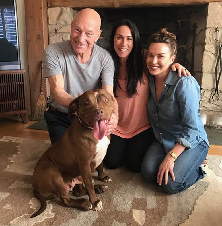 Foster Pit Bull and Patrick Stewart posing with a dog in front of a fireplace, expressing love.