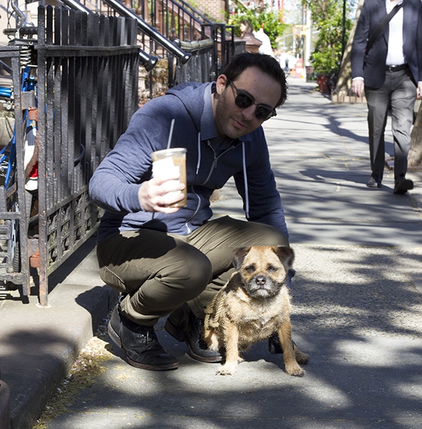 A man crouching down next to a street dog.