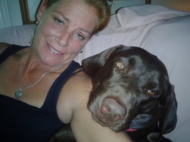 A woman is relaxing on a couch with her loyal dog by her side.