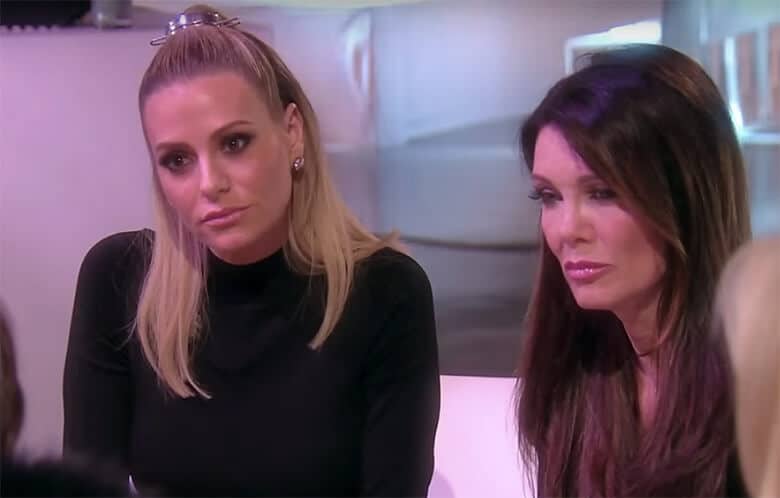 Two women, Lisa Vanderpump and another individual, sitting next to each other on a couch discussing dog drama.