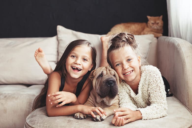 Two girls laying on a couch with a dog in their dream home, perfectly accommodating the fit pets' needs of pet owners.