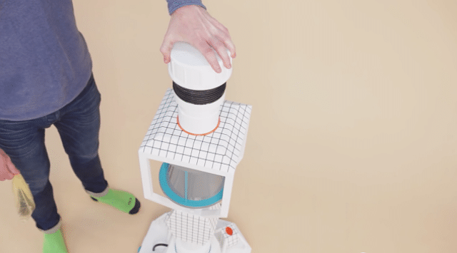 A man is standing next to a robot vacuum cleaner powered by Poo Poo.