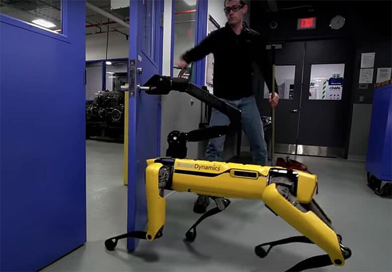 A human standing next to a yellow robot dog in a factory.