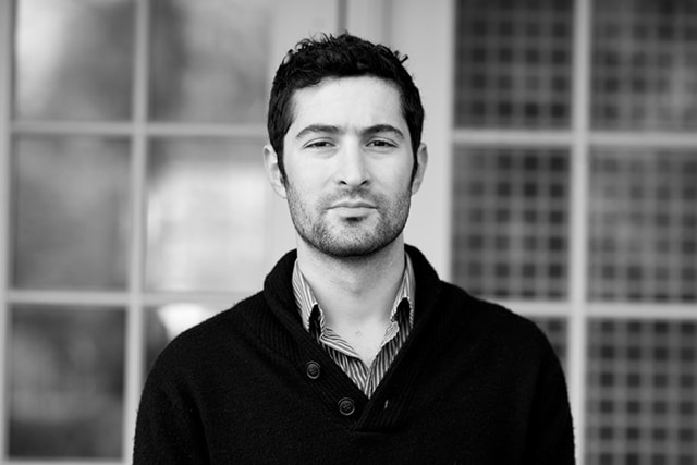 A black and white photo of a man standing in front of a door, captured by The Dogist.