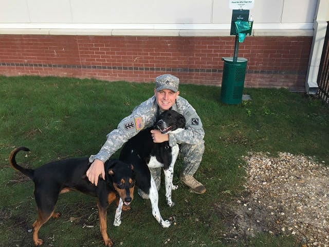 A woman is kneeling down with two dogs in front of a building, participating in the Pets for Patriots program.