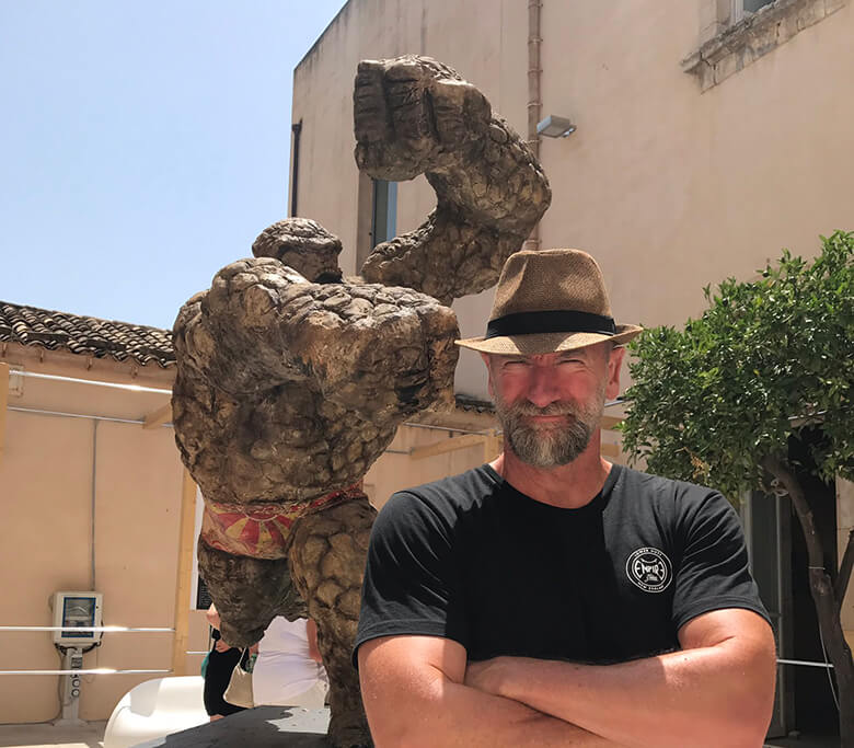 A man in a hat standing next to a statue.