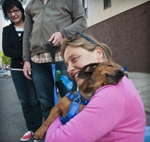 A badass woman is hugging a dog on a leash at an animal rescue in Brooklyn.