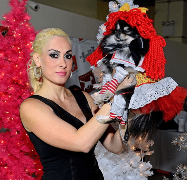 A woman in a black dress gracefully holding a small dog during a celebrity catwalk.