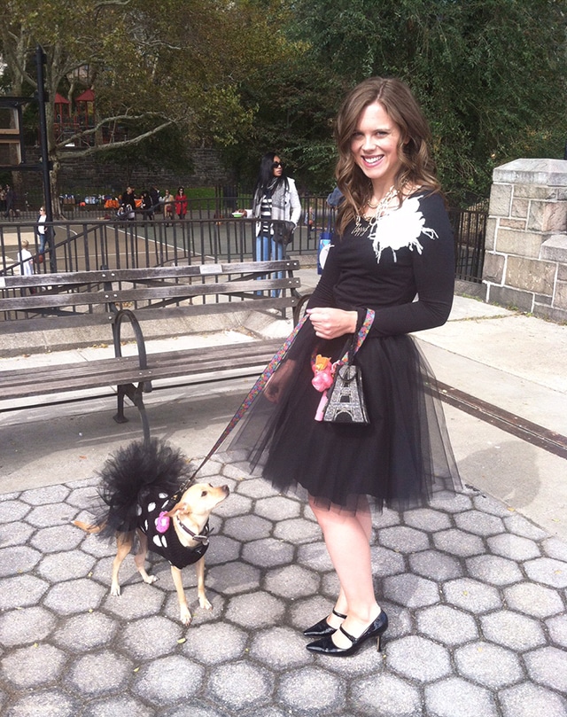 A woman dressed in a black dress and walking her dog on a leash.