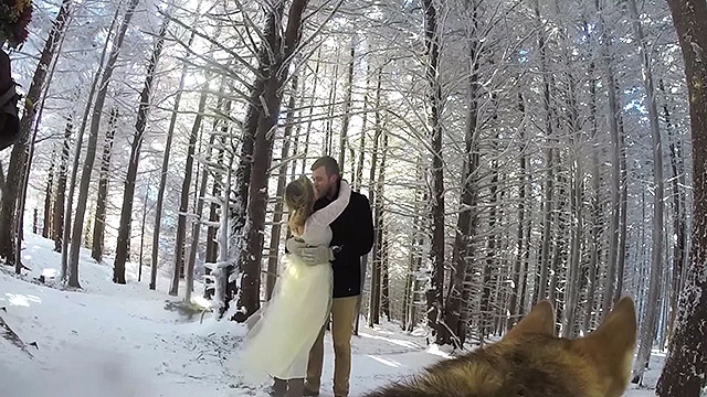 A winter wedding couple captured by a GoPro camera kissing in a snowy forest.