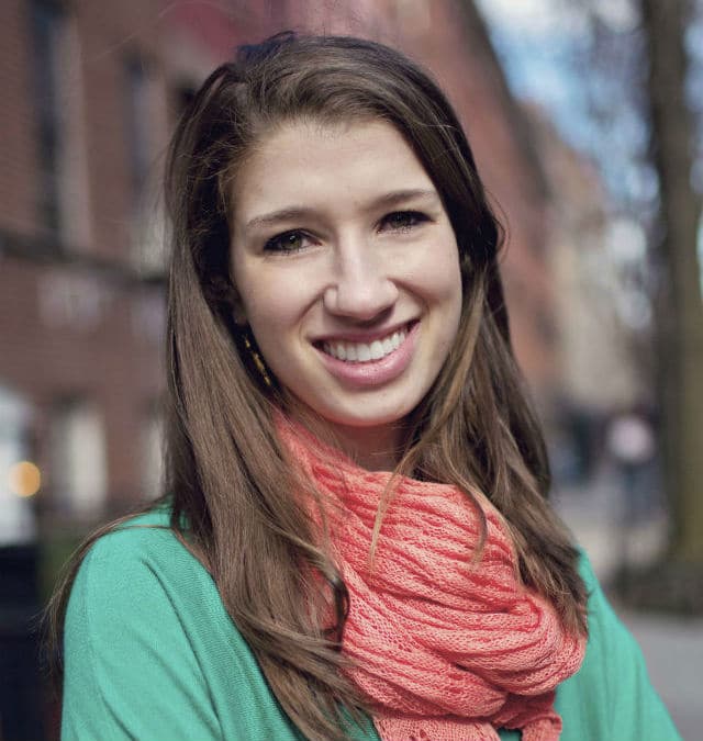 A smiling young woman in a green shirt and scarf acts as a dog matchmaker.