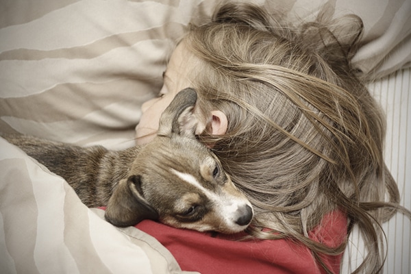 A girl surrounded by family, laying in bed with a dog.