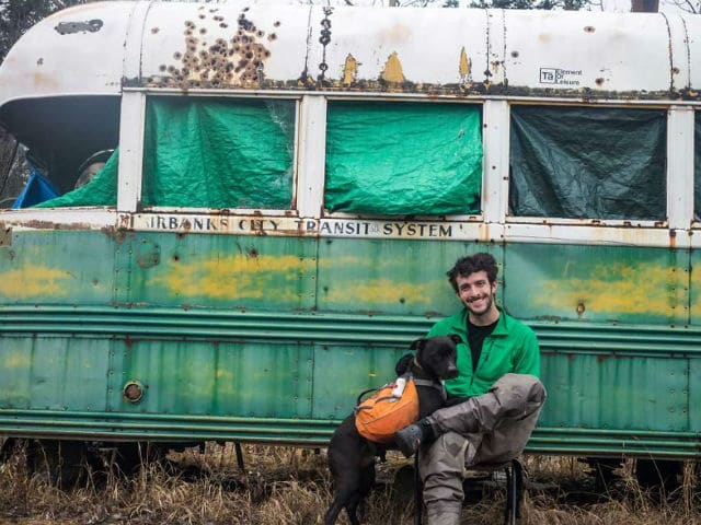 Dwayne Parton sitting in front of a green bus with a dog.