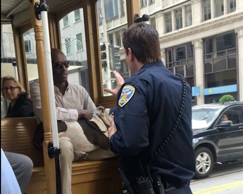 A police officer conversing with a man on a cable car while being recorded on video.