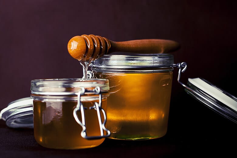 Honey is being poured into jars with a wooden spoon, emphasizing its healing benefits.