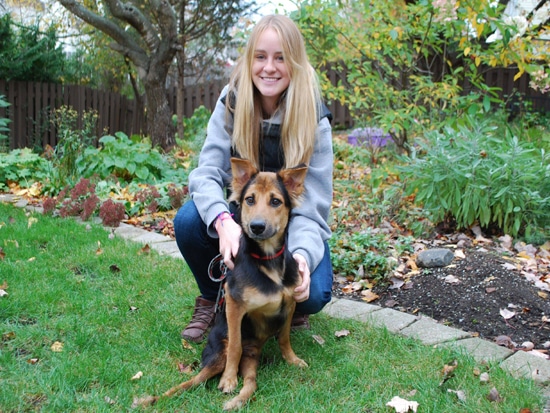 A paralyzed woman kneeling in the grass with a brown and black dog.