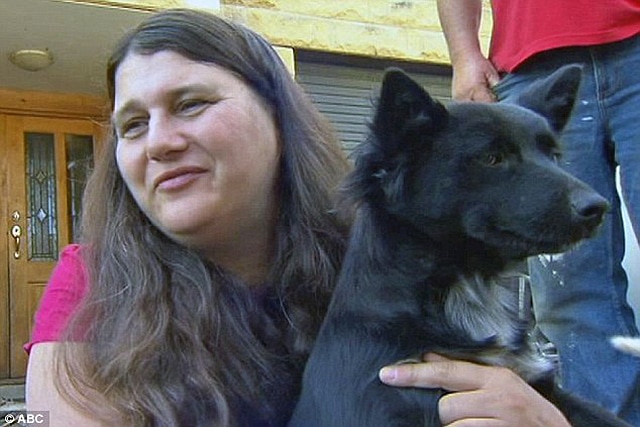 A woman holding a black dog in front of a house, showcasing the bond between pet and owner.