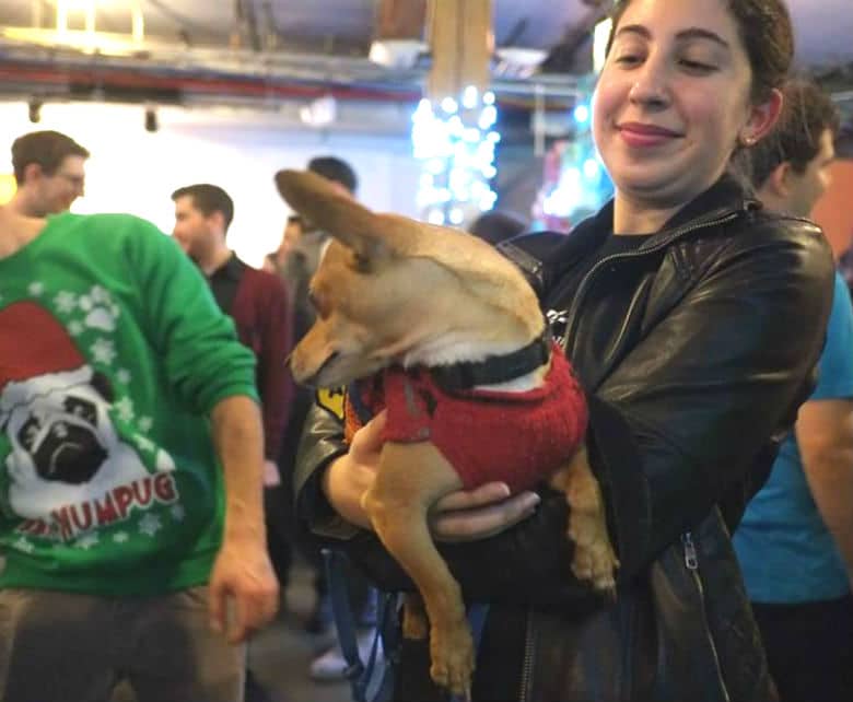 A woman holding a dog at a Christmas party surrounded by gifts.