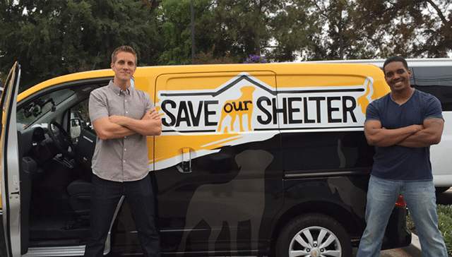 Two men standing in front of a van that says Save Our Shelter.