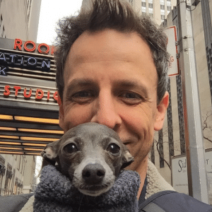 Seth Meyers is holding a small dog in his arms.