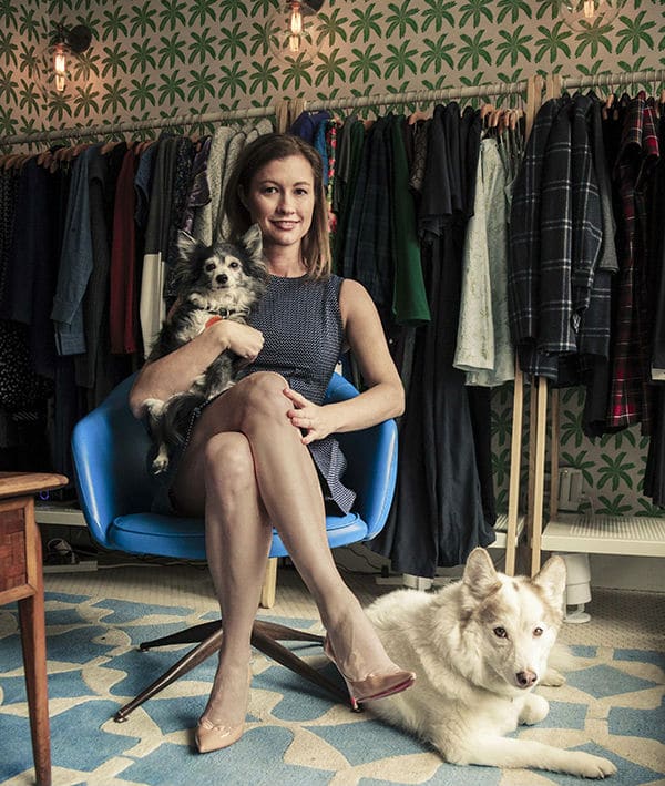 A woman sits in a chair with a dog in front of clothing racks.