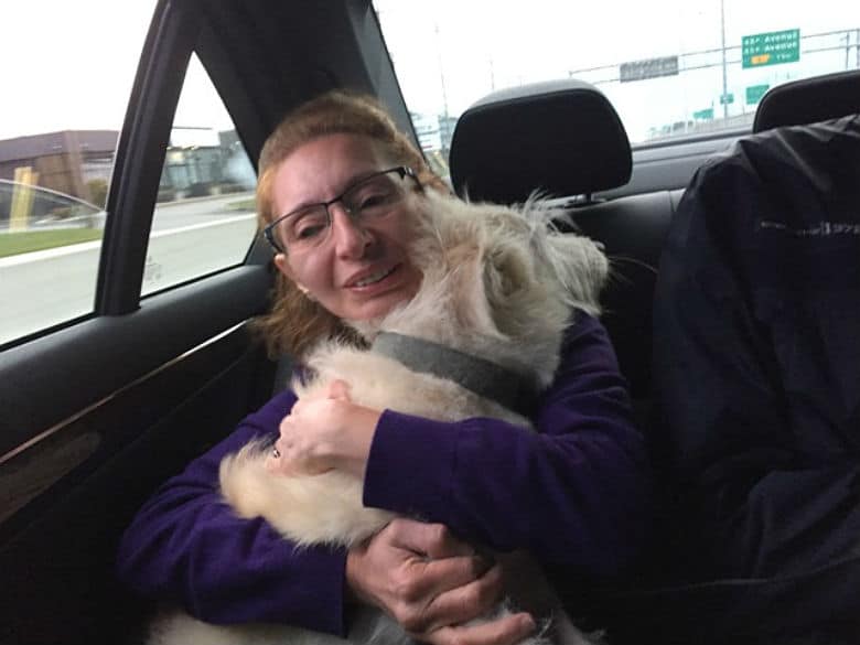 A woman is hugging her dog in the back seat of a car, comforting both herself and her beloved pet during their journey as Syrian refugees.