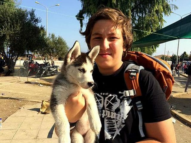 A boy from Syria with a backpack holding a husky puppy.