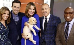 A group of people posing with a puppy on the set of the today show.