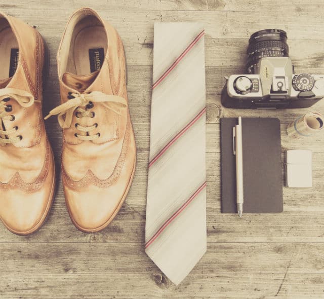 A pair of brown shoes and a camera on a wooden table.