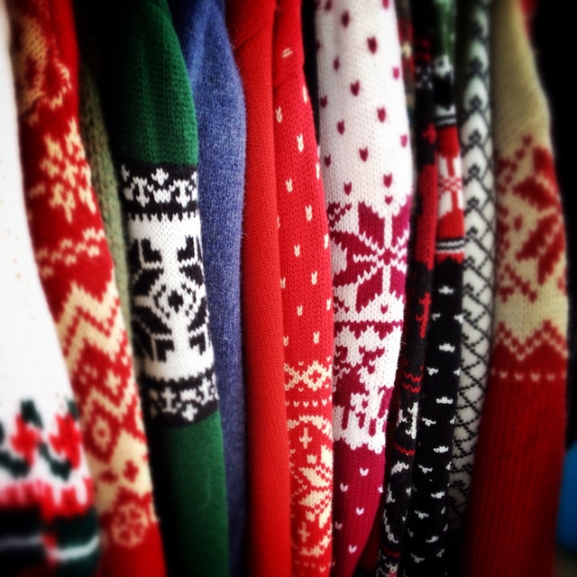 A row of ugly sweaters hanging on a rack, with a corgi patterned sweater standing out.