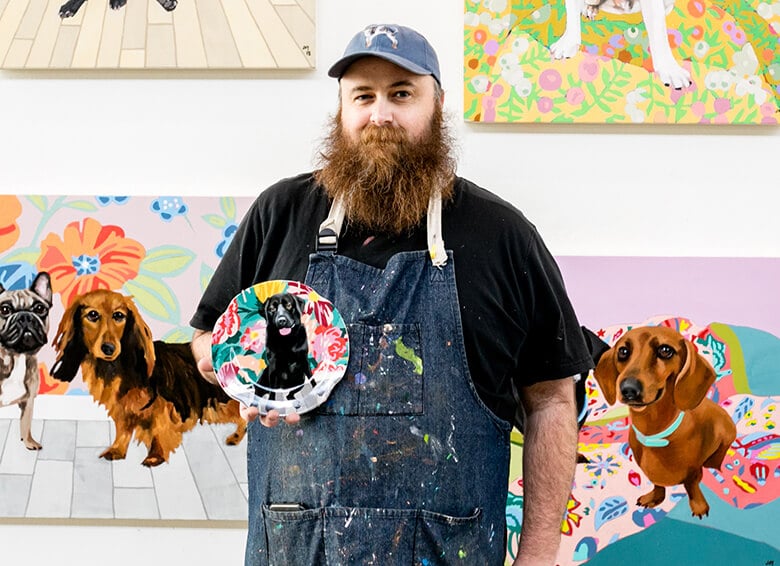 Meet an artist standing in front of paintings of dogs.