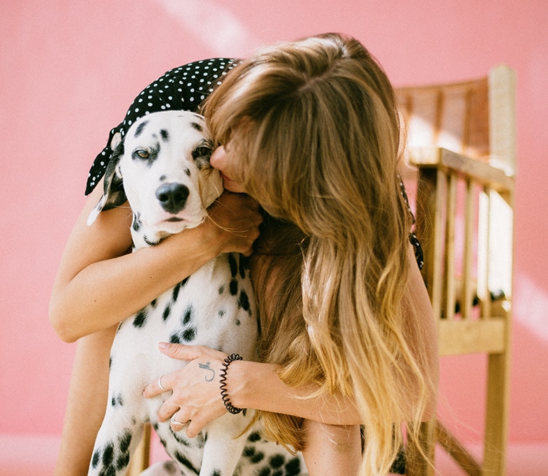 In honor of National Pet Day, a woman expresses her love for her dalmatian dog by embracing it affectionately in front of a vibrant pink wall.