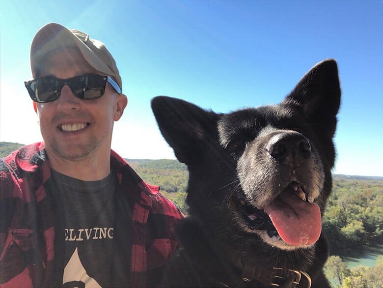 A man with a black dog standing next to a waterfall.