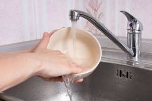 A person washing a dog's food bowl in a kitchen sink.