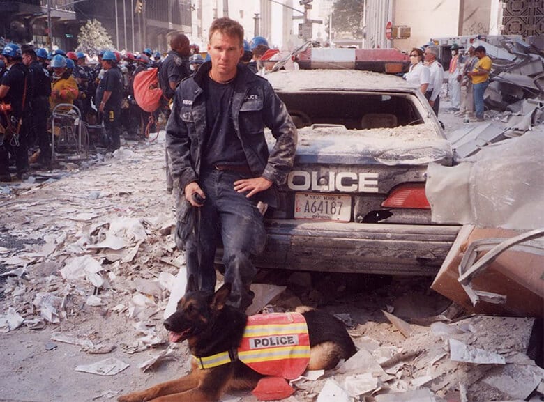 A police officer and his dog, celebrating Hero Dogs, standing next to a pile of rubble.