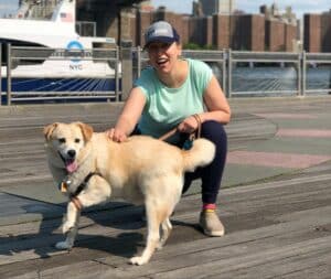 A woman kneeling on a pier with her dog, learning life lessons from her furry zen master.