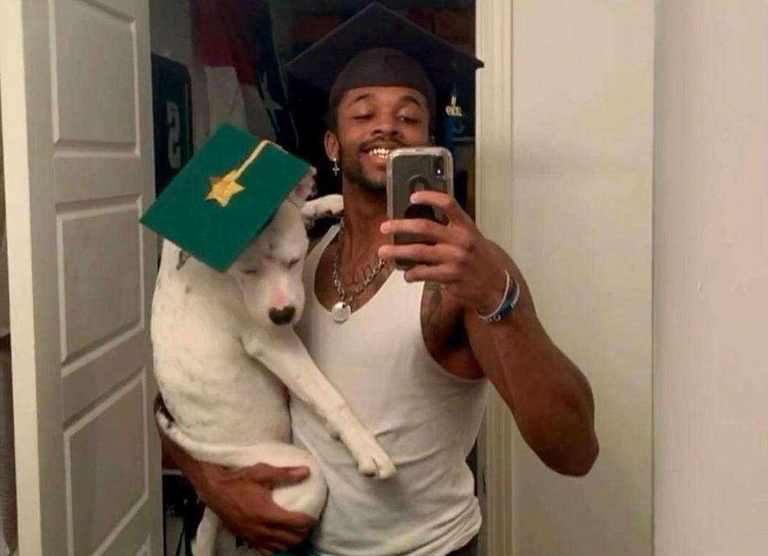 A football player taking a selfie with his rescue dog wearing a graduation cap.