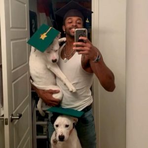 A football player wearing a graduation cap and gown with two rescue dogs.