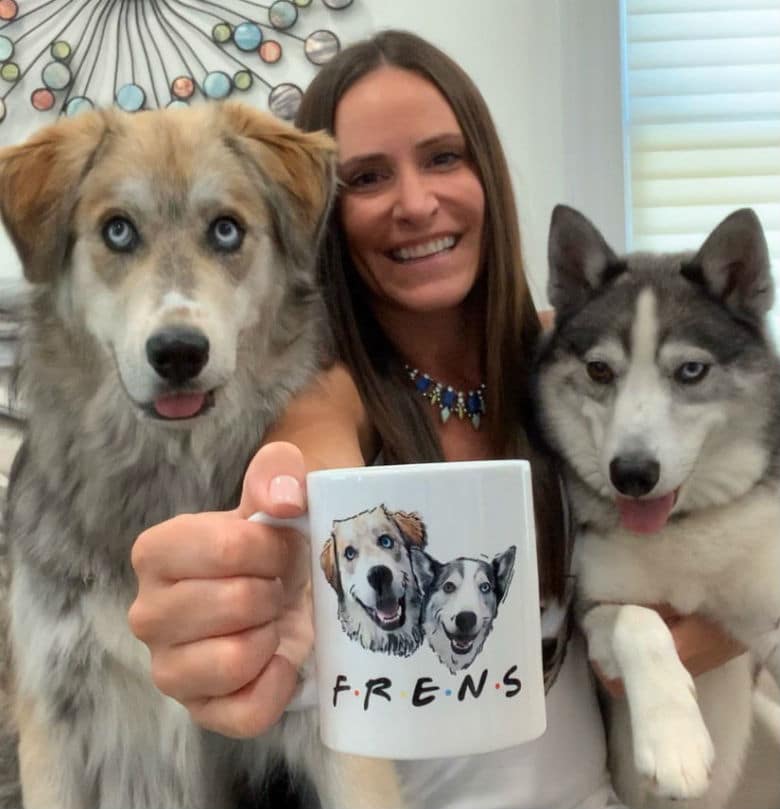 A woman holding a coffee mug with two huskies finds comfort from her dogs during the coronavirus pandemic.