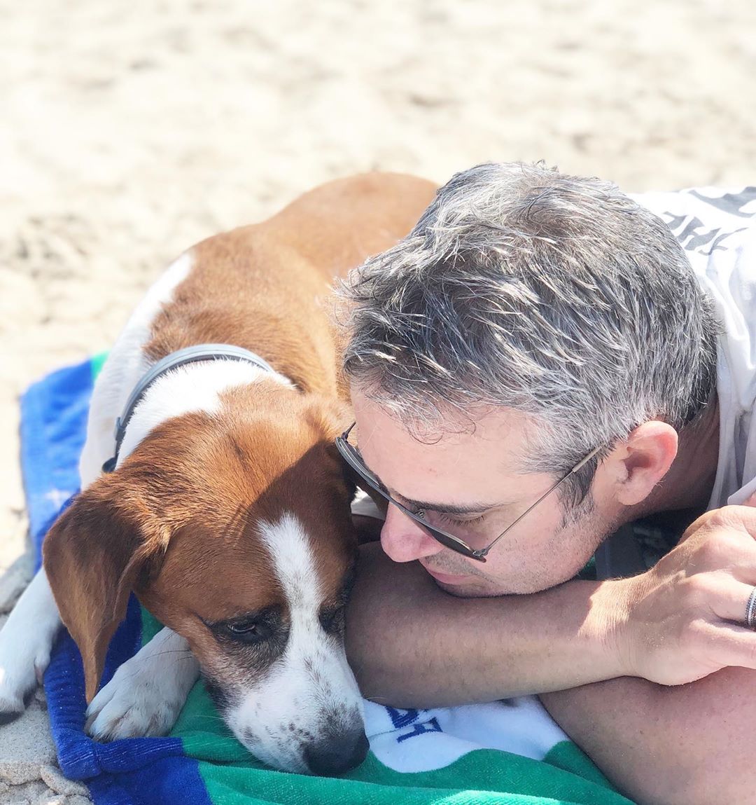 A man laying on the beach with his rescue dog. - This Dogs Life