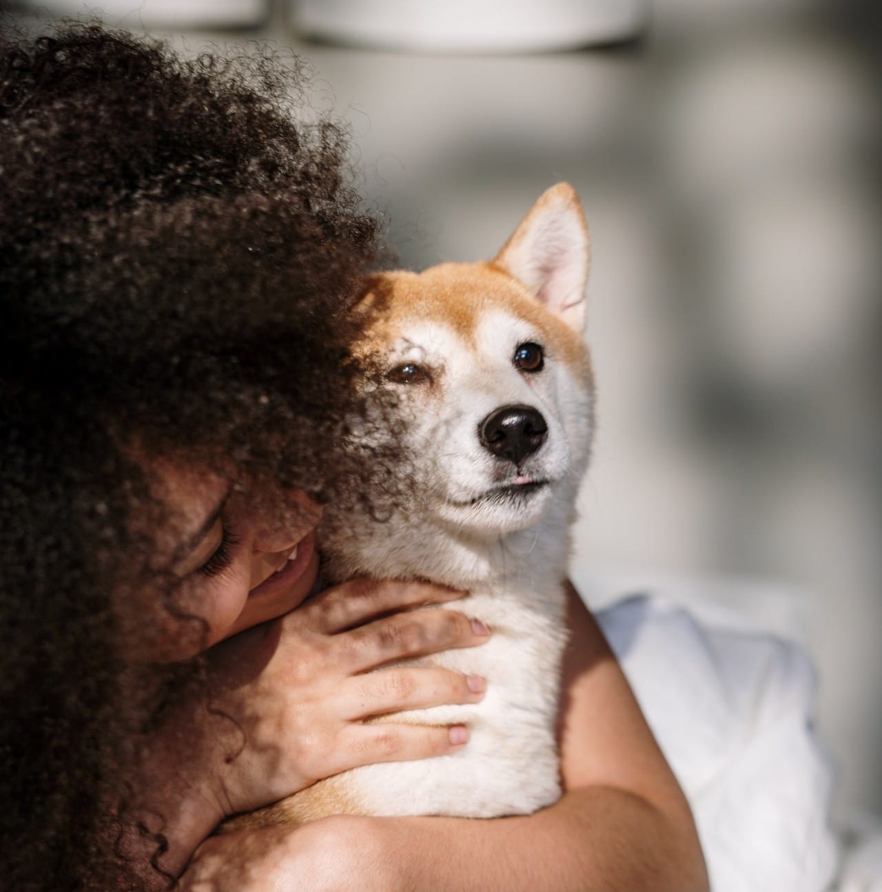 A woman hugging her dog in bed, contemplating easy ways to cut down on dog care costs.