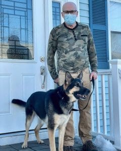 A man wearing a face mask standing next to a rescue dog german shepherd.